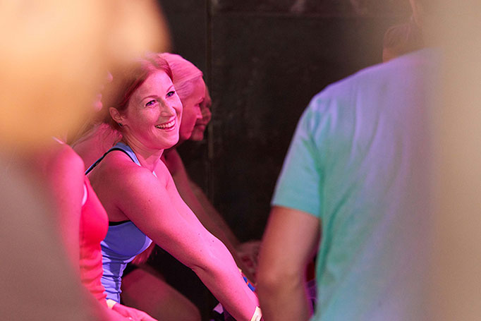 Eine Frau lächelt in rosa Veranstaltungslicht bei einem Spinnig Event von lululemon Athletica, Eventfotografie,© Florian Freund