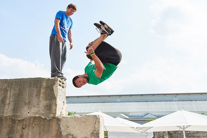 Parkour Sportler bei einer Vorführung. Einer von Ihnen macht gerade einen Salto, Veranstaltungsreportage © Florian Freund