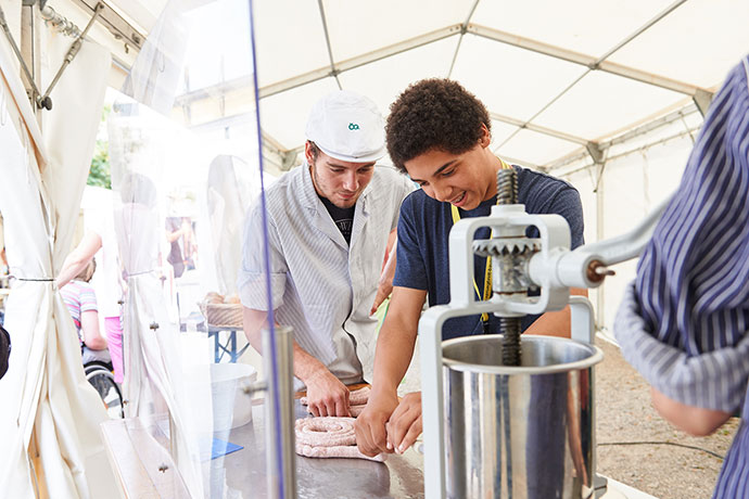 Ein Junger Mensch darf bei einer Veranstaltung von Sprungbrett Bayern unter fachkundiger Anleitung selbst Wurst herstellen. Veranstaltungsfotografie, © Florian Freund
