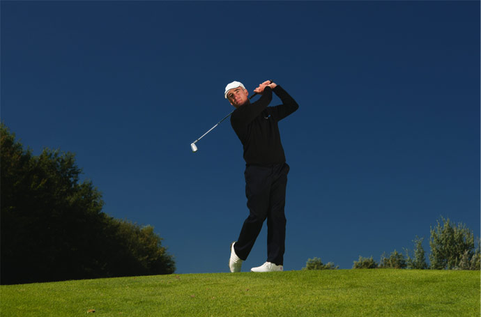 Ein Golfspieler steht auf dem Rasen vor einem tiefblauen Himmel und hohlt zum Schlag aus, Peoplefotografie © Florian Freund